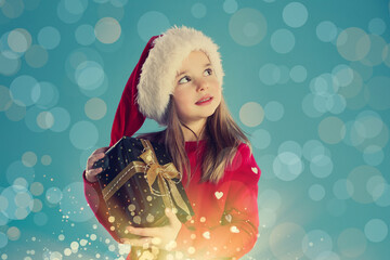 Canvas Print - Cute child in Santa hat with Christmas gift on light blue background