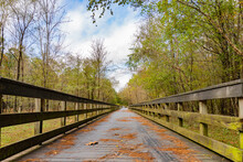 Leading Lines Of A Wooden Bridge Leading Over A Creek And Surrounded By Trees Under A Cloudy Blue Sky On The Neuse River Greenway In Raleigh., North Carolina, USA