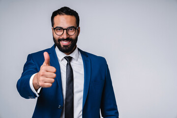 Wall Mural - Cheerful young middle eastern businessman showing thumb up isolated over grey background