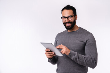 Wall Mural - Side view photo of young handsome arab man using tablet in casual outfit isolated over white background