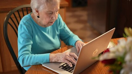overhead view of elderly woman sitting at dining room table and working on laptop computer with tea.