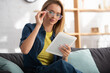 © LIGHTFIELD STUDIOS - blonde woman touching eyeglasses while looking at digital tablet at home on blurred background