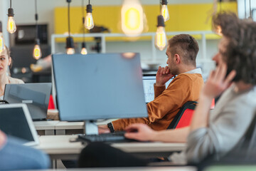 Bearded employee guy with afro haircut talking on his phone while being surrounded by his multiethnic coworkers. Businessman working in a casual startup modern environment.