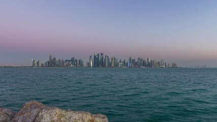 Wall Mural - Skyline of the arabian city of Doha night to day transition timelapse in Qatar, captured in the very early morning before sunrise with illuminated skyscrapers. View from Corniche Promenade