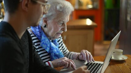 Extreme closeup of elderly senior woman learning to use a laptop computer from teen male grandson with tea.