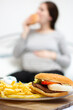 © Ersin - young hungry pregnant woman eating a hamburger and fried potatoes. Concept of unhealthy nutrition during pregnancy, Mother waiting baby. Close-up of belly and junk food (fast food).
