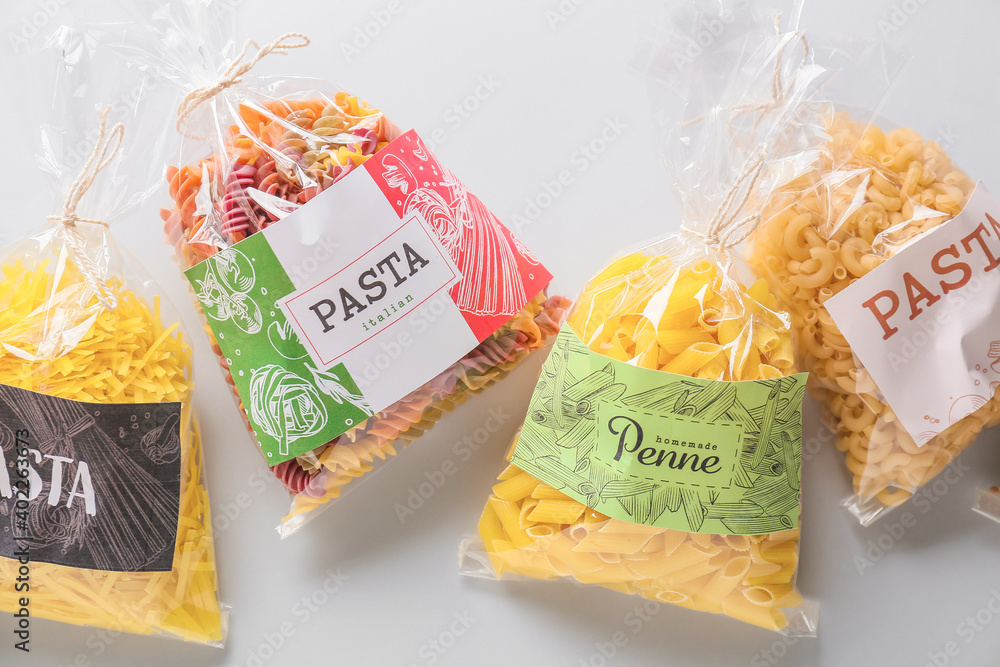 Bags with uncooked pasta on white background