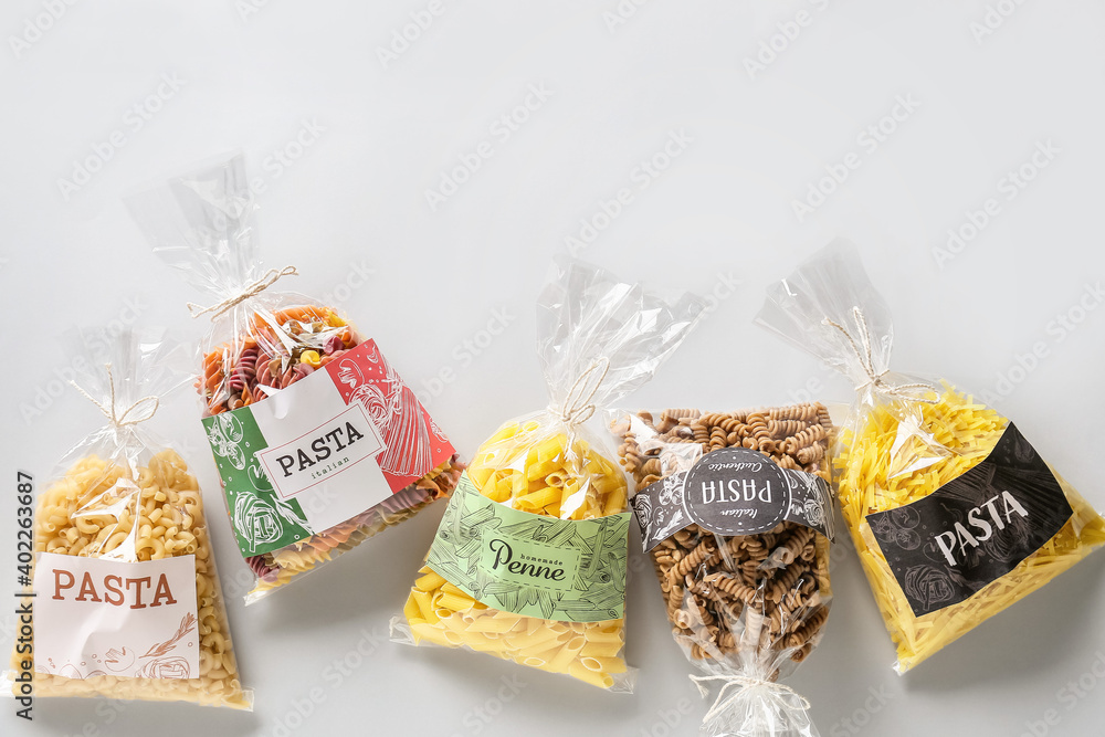 Bags with uncooked pasta on white background