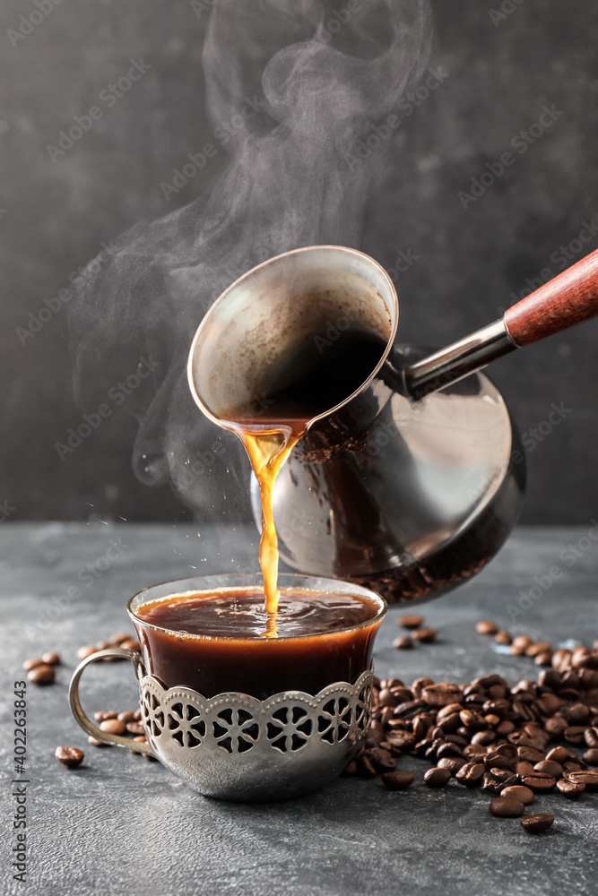 Pouring hot coffee from cezve in cup on table
