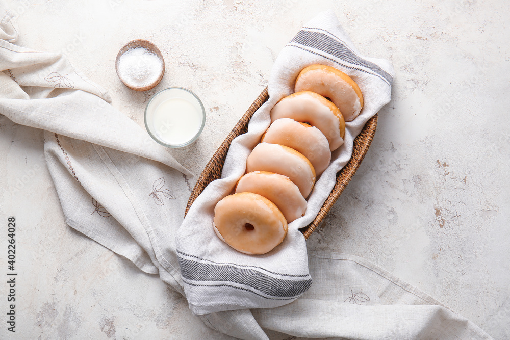 Tasty donuts in wicker basket on light background