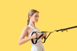 © Pixel-Shot - Sporty young woman training with TRX straps on color background