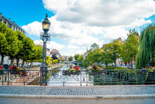 Scenic View Of A Bridge With A Historic Street Lamp, Flower Boxes In The Front And A Beautiful River Canal In The Background.