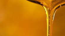 Pouring Oil Or Honey Drop On Golden Background. Macro Shot.