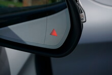Close up of illuminated blind spot monitor warning on door mirror of modern luxury car.