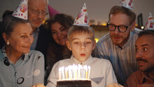 Cute Boy Blowing Out Birthday Cake Candles At Family Party