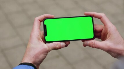 Hand man holding a smartphone touching phone with horizontal green screen phone on background street. Message business male device digital equipment internet. Slow motion