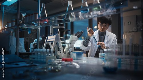 Medical Development Laboratory: East Asian Scientist Uses Micro Pipette for Filling Test Tubes with Liquid, Conducting Experiment. Pharmaceutical Lab for Research Medicine, Biotechnology. Evening Work