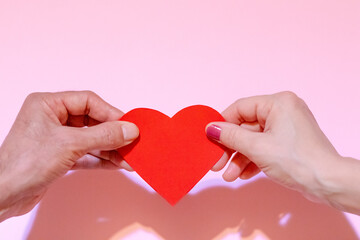 couple holding a heart against pink background, valentines day and love concept, Two hands holding a red heart shape card on pink background.