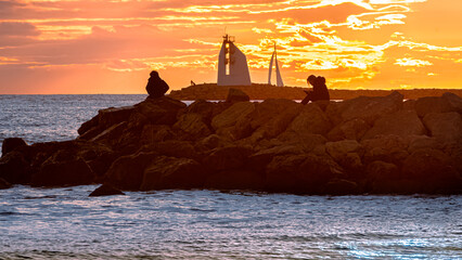 Wall Mural - Vue de deux silhouettes de personnes en contre-jour avec un coucher de soleil sur une digue avec vue du phare de La Grande Motte, sud de la France près de la Camargue.