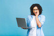 © denis_vermenko - Shocked amazed african american black business or student woman, posing isolated on blue background. Mock up copy space. Working on laptop pc computer.