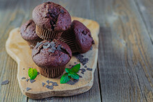 Fresh Homemade Chocolate Muffins Or Cupcakes On A Wooden Board On A Rustic Wooden Background With Fresh Green Mint Leaves. Place For Your Text. Bakery, Bakery