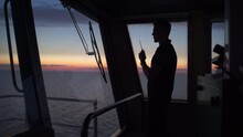 Silhouette Of A Ferry Boat Officer Talking At A VHF Nautical Radio With A Sunset In The Background