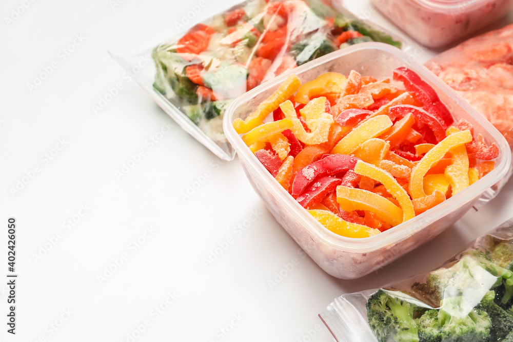 Container and plastic bags with frozen vegetables on white background