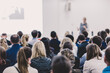 © kasto - Business and entrepreneurship symposium. Female speaker giving a talk at business meeting. Audience in conference hall. Rear view of unrecognized participant in audience. Copy space on whitescreen.