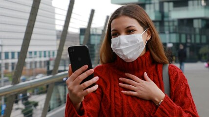 Wall Mural - Euphoric surprised young woman video calling with smartphone in city street using the protective mask