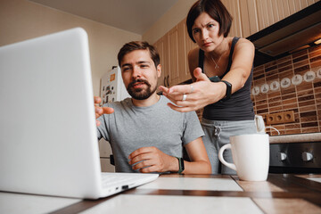 Couple at kitchen, reading news and using laptop.