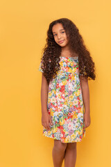 Young dark skinned young girl with long curly hair wearing colorfull dtress on a yellow background