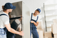 Indian Mover Looking At Coworker While Moving Fridge In Apartment
