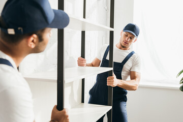 Wall Mural - young mover carrying heavy rack with indian coworker on blurred foreground