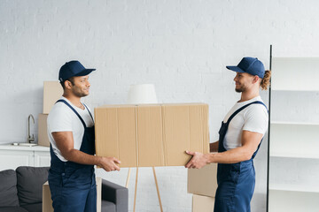 Wall Mural - side view of multiethnic movers looking at each other and holding carton box