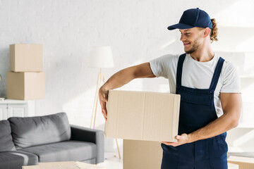 Wall Mural - positive mover in cap and uniform holding carton box in apartment