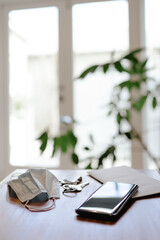 Table desk with protective mask, keys, mobile and a letter in entrance of a house. Vertical