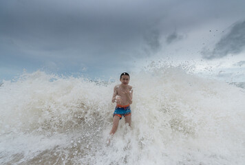 An Asian boy has felt happy and fun on the beach with a cloudy sky.