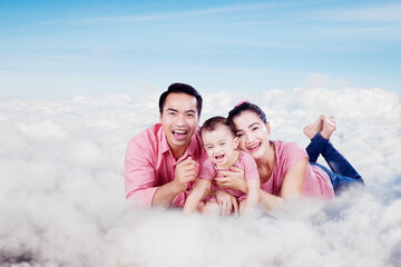 Wall Mural - Happy parents lying with their baby over clouds