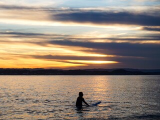 Wall Mural - A silhouette of a male surfer sat on his board as the sun sets behind him - Gold Coast, Australia