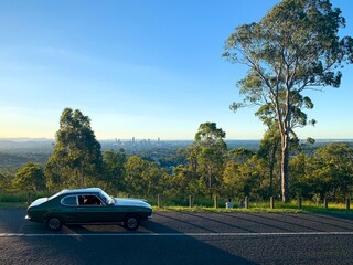 A classic car drives along a road infront of the city skyline - Brisbane, Australia