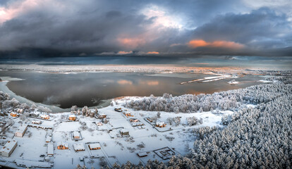 Wall Mural - Sunrise over a snowy valley with river flowing through the forest in Sigulda. Aerial view with dark storm clouds.