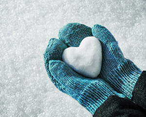 Female hands in knitted mittens with heart of snow in winter day. Love concept. Valentine day background.