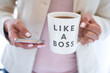 © Julia - Business woman using mobile phone and holding cup that says Like A Boss