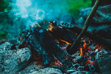 Vivid Smoldered Firewoods Burned In Fire Close-up. Atmospheric Warm Background With Orange Flame Of Campfire And Blue Smoke. Wonderful Full Frame Image Of Bonfire. Burning Logs In Beautiful Fire.