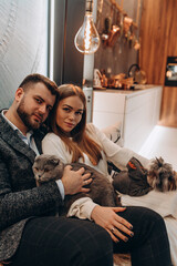 Poster - Young married couple in a cozy home environment. On the hands of a gray cat. Studio photography.