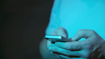 Close up of human hands holding smartphone in blue neon light on night street, typing and using apps to pay via internet banking, communicating via social media app and looking for information