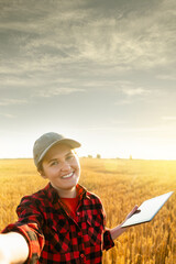 Poster - Woman farmer with digital tablet makes selfie on the background of a wheat field.	