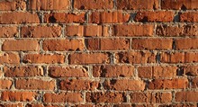 Fragment Of A Brick Wall With Uneven Masonry Of Bright Orange Blocks With Light Concrete Seams, Full Frame Abstract Textured Brick Background Illuminated By Soft Sunlight