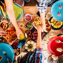 Vertical view of group of friends family eating together on a wooden table full of food - people celebrating and enjoying lunch in friendship and having fun - colored background traditional dinner