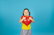 © Юля Бурмистрова - a happy child in a yellow T-shirt hugs a red heart-shaped balloon and gives a thumbs up isolated on a blue background.